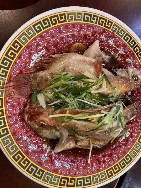 Whole steamed fish on traditional red plate